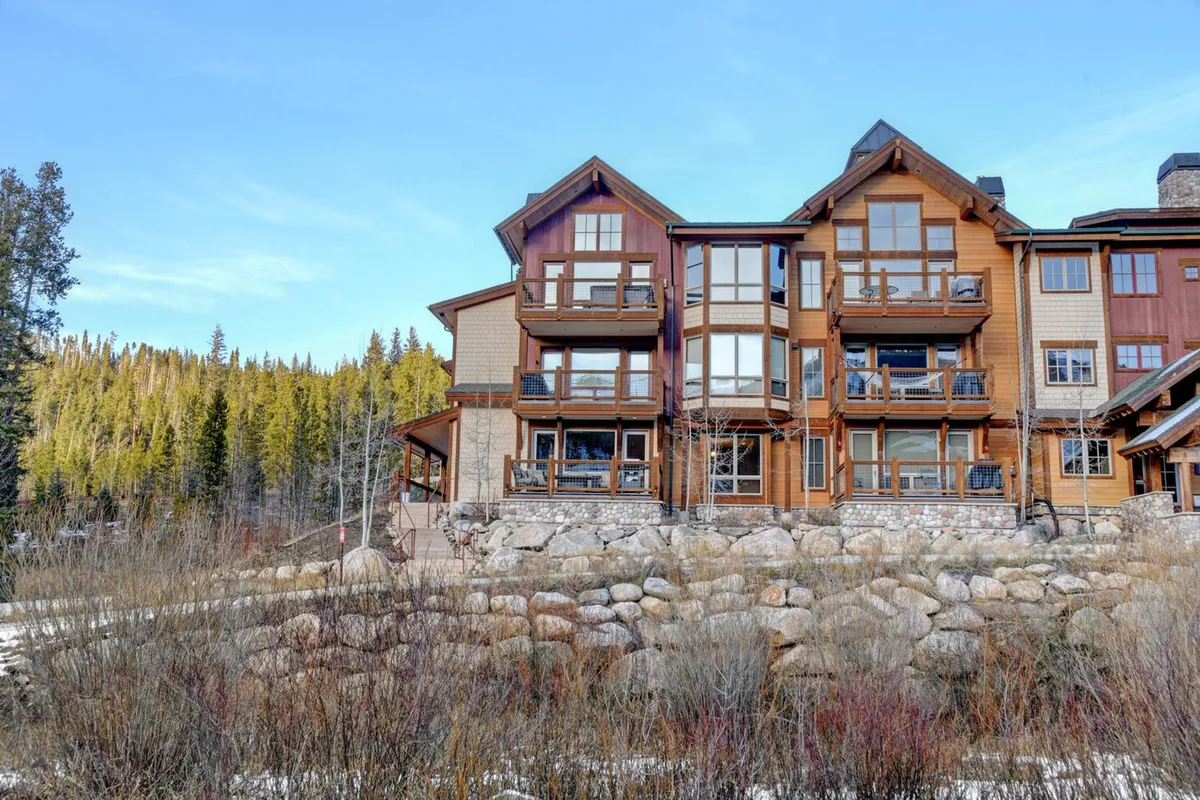 This exterior image features the building's multi-level architecture with large windows and natural stone landscaping, set against a serene natural backdrop. The scene conveys a sense of tranquility and pristine surroundings.