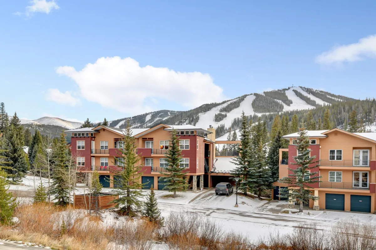 This image captures a vibrant winter scene with a snow-covered landscape, colorful alpine buildings nestled among pine trees, and a dramatic mountain backdrop. The area looks lively, ideal for skiing, snowboarding, and après-ski relaxation.