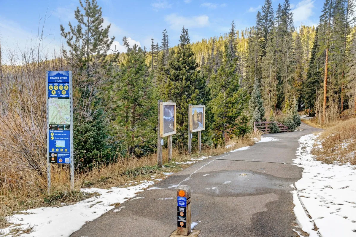 A paved pathway winding through the trees, with informational boards and a tranquil natural setting, suggesting immediate access to outdoor adventures like hiking or biking along the Fraser River Trail.