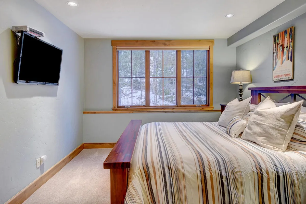 This image showcases a comfortable bedroom with a bed, window, lamp, and wall-mounted TV. Soft lighting and plush bedding create a cozy, inviting environment, with thoughtful details that reflect comfort and tranquility.