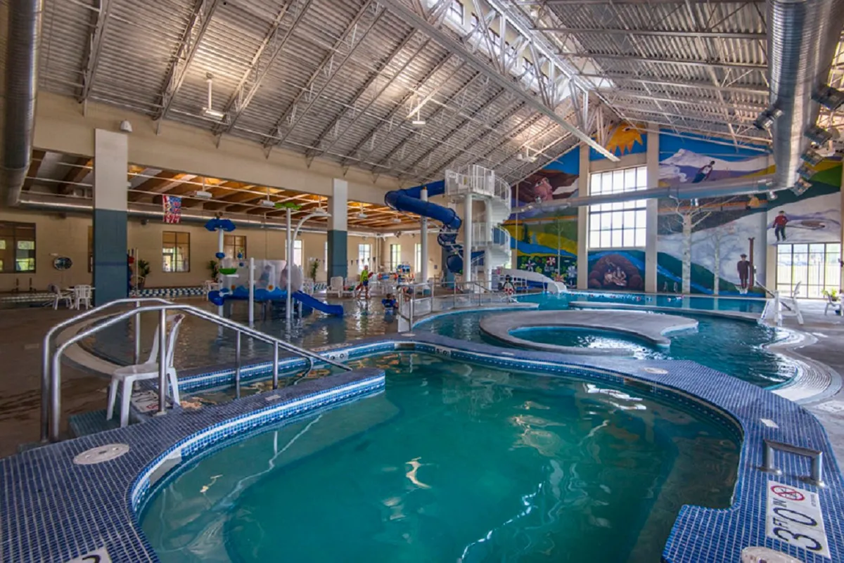 A cheerful indoor recreation setting showing children playing on water slides, a colorful pool area, and families enjoying vibrant aquatic activities. The area is filled with laughter and playful energy, perfect for family outings and special occasions.