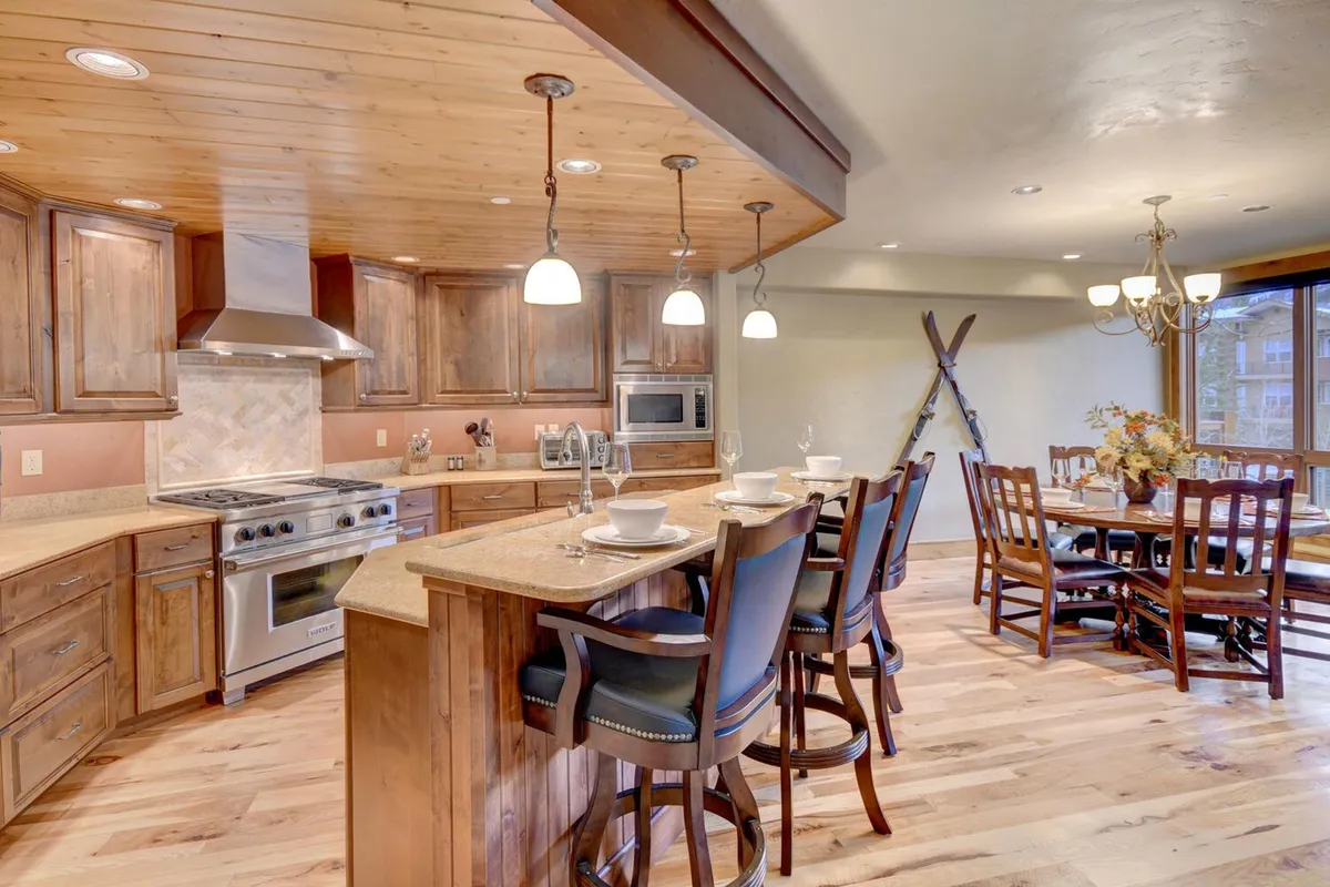 This image captures a view of the kitchen and adjoining dining area. The kitchen island and wooden cabinetry are complemented by stylish lighting fixtures, and the dining table is close by, creating a seamless flow for socializing and meals.