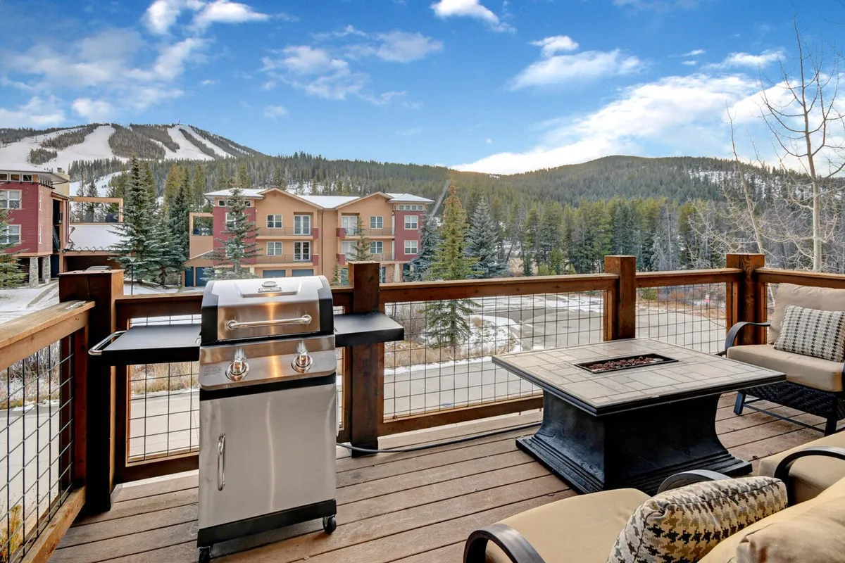 A private deck featuring a BBQ grill, outdoor seating, and a stunning view of the mountains. The space is set up for barbecuing, relaxing, and socializing, with the scenic alpine backdrop enhancing the experience.